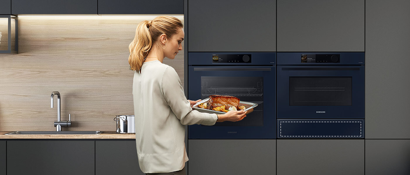 Zdjęcie przedstawia szarą zabudowę kuchenną, w którą zostały wstawione dwa piekarniki wraz z szufladą podgrzewającą Samsung