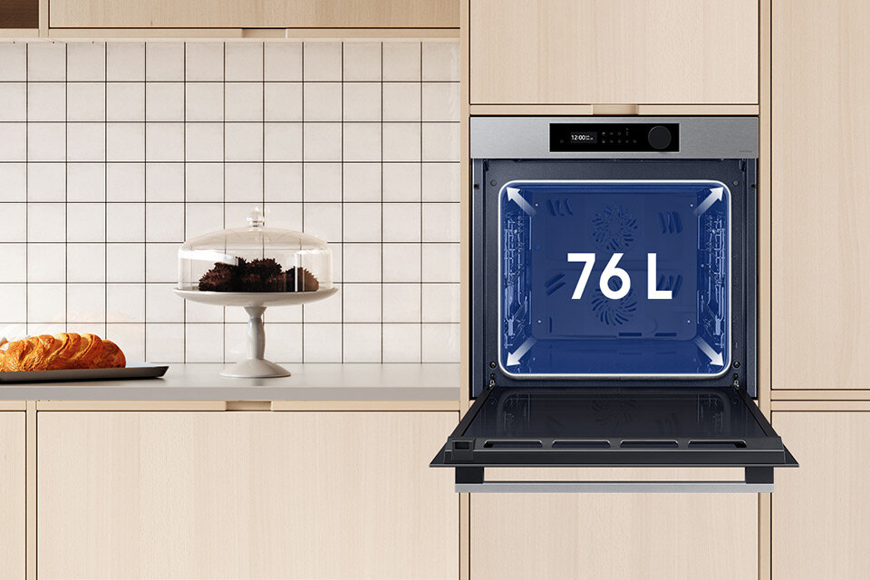 Zdjęcie przedstawia pojemne wnętrze piekarnika Samsung NV7B5645TAS, który został wstawiony do kremowego pomieszczenia kuchennego.